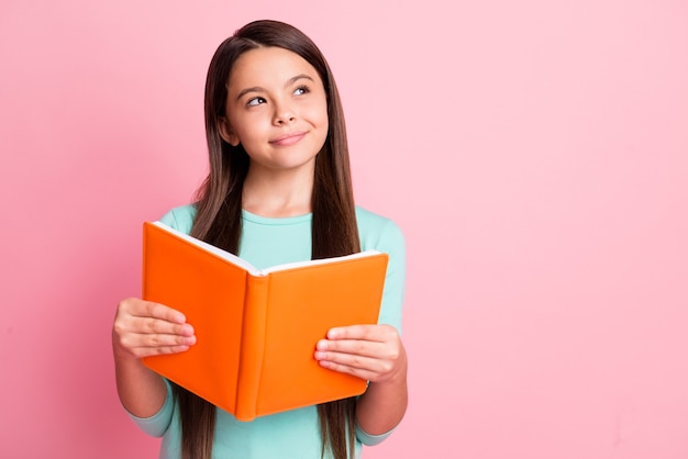 Foto van mooie lieve kleine zware latijnse dame lange kapsel armen houden oranje boek sluw opzoeken lege ruimte doordachte slijtage turquoise groenblauw sweatshirt geïsoleerde roze kleur achtergrond