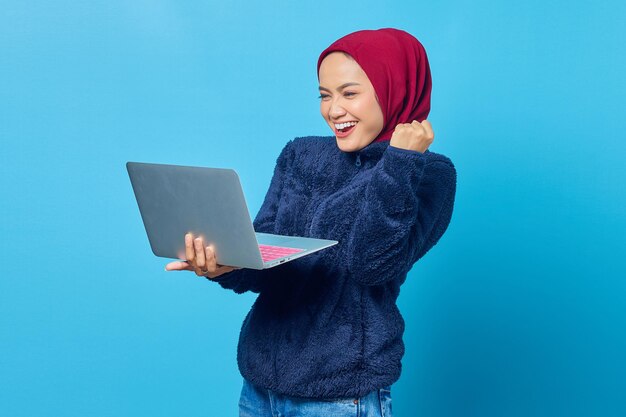 Foto van opgewonden Aziatische vrouw die inkomende e-mail op laptop over blauwe achtergrond bekijkt