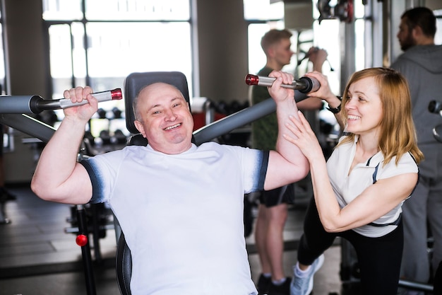 Foto van ouder echtpaar in de sportschool. Een man doet een oefening op zijn armen en schouders.