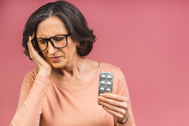 Foto van oudere volwassen bejaarde senior vrouw blij met een positieve glimlach met medicijnen pillen geïsoleerd over roze kleur achtergrond.