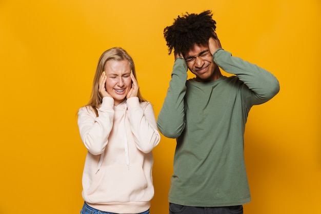 Foto van overstuur paar man en vrouw 16-18 met beugels die oren bedekken, geïsoleerd op gele achtergrond