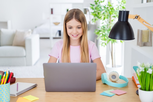 Foto van positief kind meisje studeren op afstand zit bureau tafel gebruik laptop heb online communicatieles met tutor die binnenshuis rapport schrijft