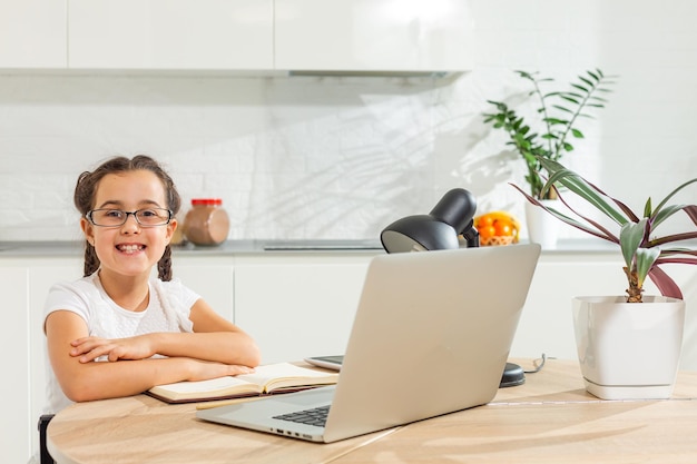 Foto van positief kind meisje studeren op afstand zit bureau tafel gebruik laptop heb online communicatieles met tutor die binnenshuis rapport schrijft