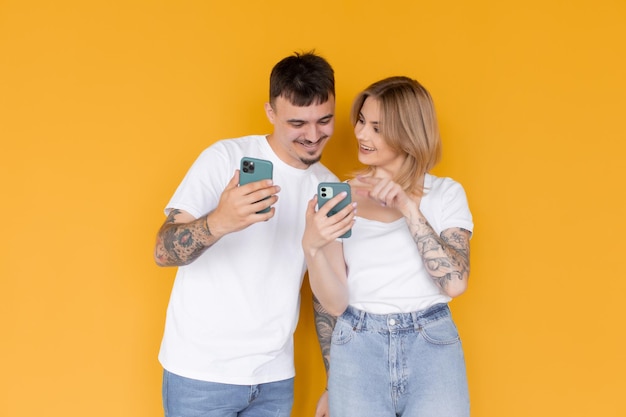 Foto van positief opgewonden mensen, man en vrouw die mobiele telefoons gebruiken, geïsoleerd over geel