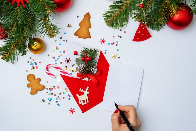 Foto van rode kerst envelop, koekjes, handen met pen, takken van sparren kerstversiering op lege witte achtergrond