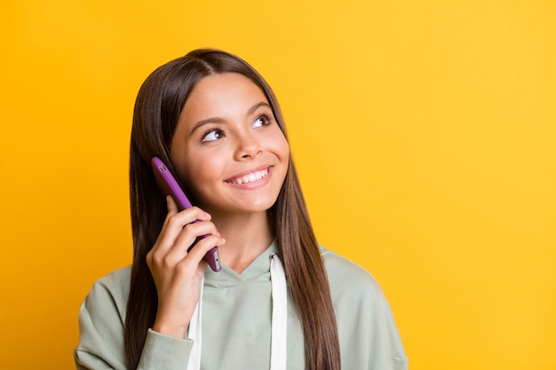 Foto van schattig positief schoolmeisje draagt een casual grijze outfit die praat met een moderne gadget die eruitziet als een lege ruimte, een geïsoleerde gele achtergrondkleur