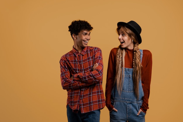 Foto van schattige boerenpaar kijken samen blij en verrast. Zwarte man draagt geruite overhemd, blanke vrouw draagt denim overall en hoed geïsoleerd bruine kleur achtergrond.