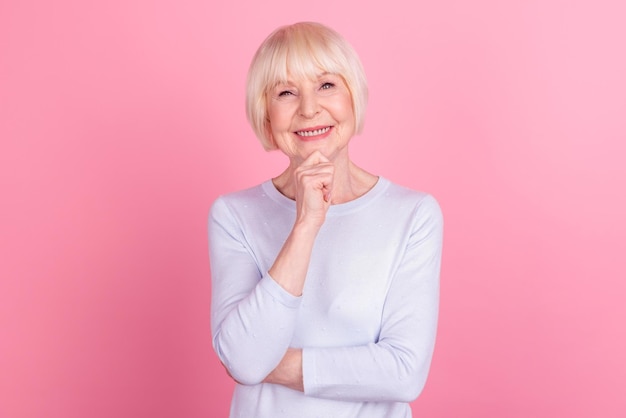 Foto van senior vrolijke vrouw goed humeur hand touch kin zelfverzekerd denk slim geïsoleerd over roze kleur achtergrond