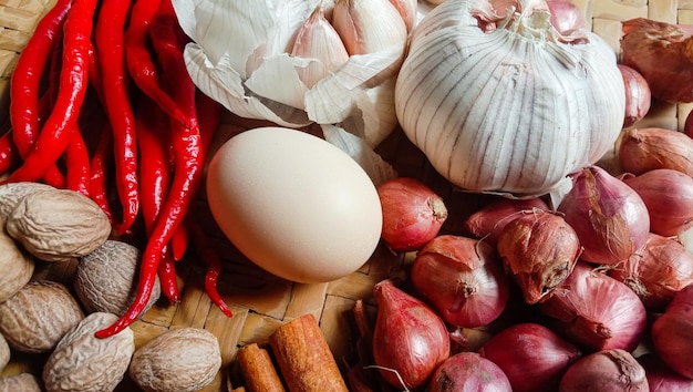 Foto van specerijen in de vorm van schaloten, knoflook, chili's en eieren gerangschikt in een geweven bamboe