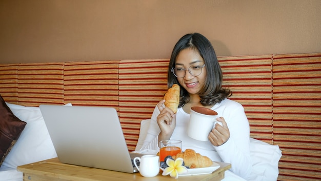 Foto van toeristen die ontbijt eten en laptop gebruikt op het bed in de luxe hotelkamer, gezond voedselconcept.