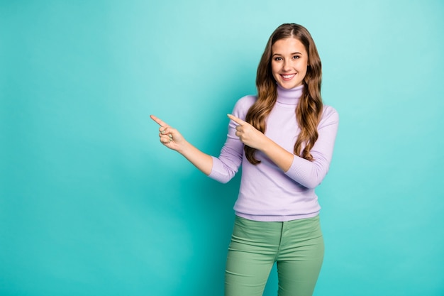 Foto van verbazingwekkende grappige mooie dame geven vingers lege ruimte aanbieding nieuwigheid product verkoop prijzen dragen paarse trui groene broek geïsoleerde groenblauw pastelkleur