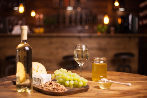 Foto van verschillende wijnsnacks op houten tafel in een vintage pub. Druiven. Honing pot. Walnoten.