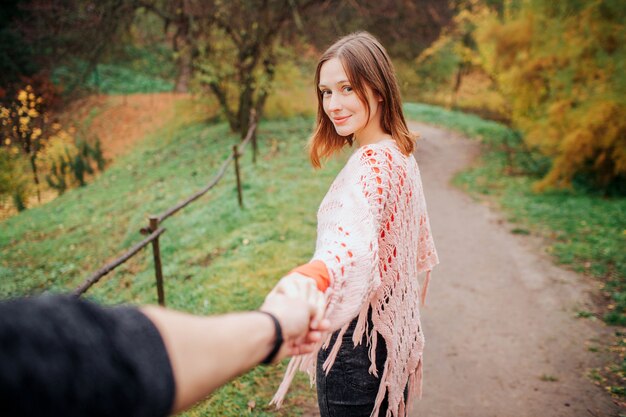 Foto van volg mij stijl. Ze houdt zijn hand vast en kijkt naar de camera. Jonge vrouw glimlacht.