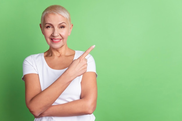 Foto van volwassen vrouw geeft aan dat vinger lege ruimte adverteert, suggereert promotie geïsoleerd over groene kleur achtergrond.