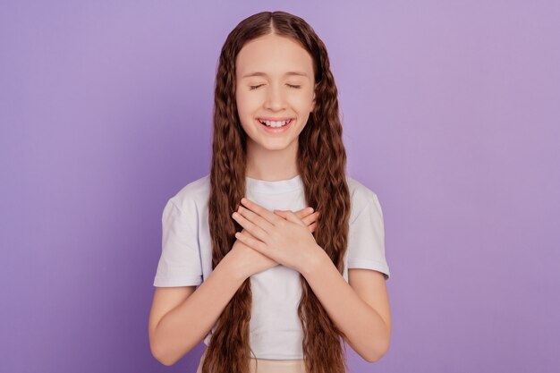 Foto van vreedzaam schattig klein meisje houdt handen hart geïsoleerd op paarse achtergrond