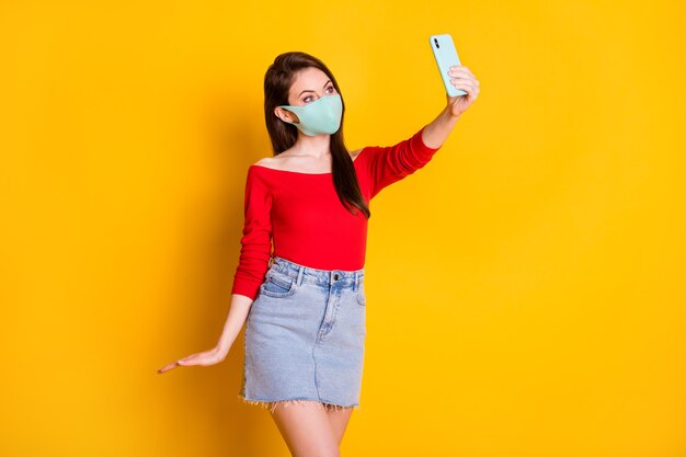 Foto van vreugdemeisje in medisch masker gebruik smartphone maak selfie covid quarantaine draag rode top korte minirok geïsoleerd over heldere glans kleur achtergrond