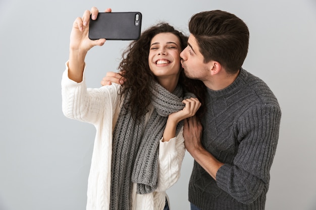 Foto van vrolijke man en vrouw die selfiefoto op smartphone nemen, die over grijze muur wordt geïsoleerd