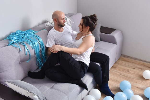 Foto van vrolijke romantische Kaukasische familie paar glimlachend en knuffelen zittend op de bank thuis. Man en vrouw verliefd