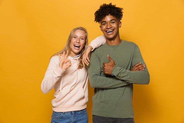 Foto van vrolijke studenten man en vrouw 16-18 met beugels die lachen en gebaren naar de camera, geïsoleerd op gele achtergrond