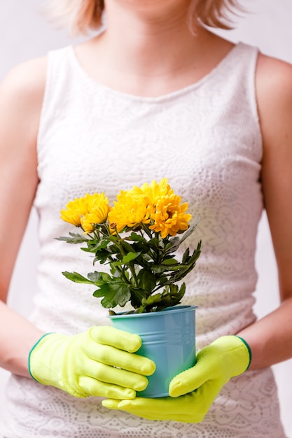 Foto van vrouw in rubberhandschoenen die pot met gele bloem houden