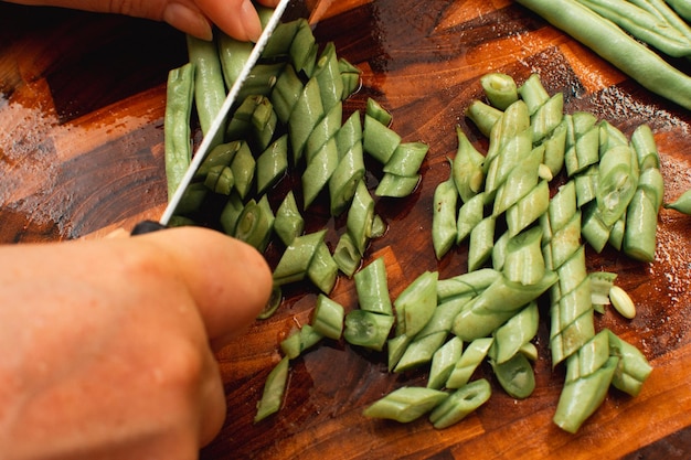 Foto van vrouwelijke hand hakken sperziebonen op houten snijplank om te koken