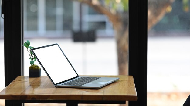 Foto van witte lege laptop van de het schermcomputer die op houten bureau met ingemaakte installatie over moderne bureau glasmuur zet