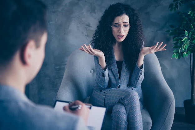 Foto van zakelijke dame zitten in stoel praten met psycholoog op betonnen muur achtergrond