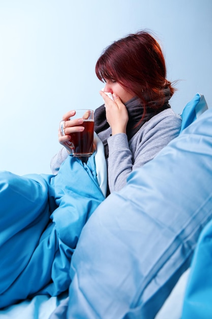 Foto van zieke brunette met kopje thee zittend in bed