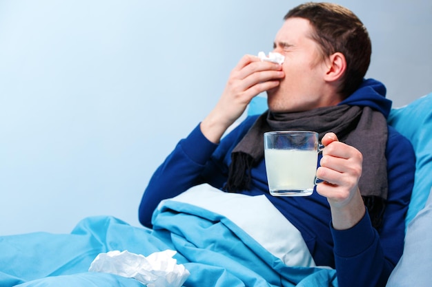 Foto van zieke man in sjaal met kopje medicijnen liggend in bed