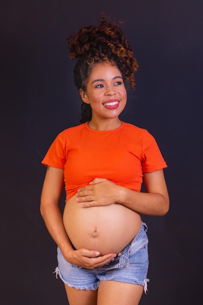 Foto van zwangere Afro-Amerikaanse vrouw gemaakt in fotostudio met zwarte achtergrond