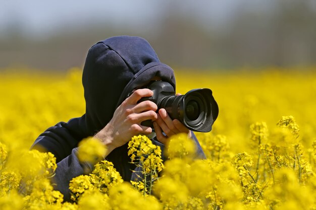 Fotograaf geschoten met een camera in zijn handen zittend in een veld met bloeiende koolzaad.