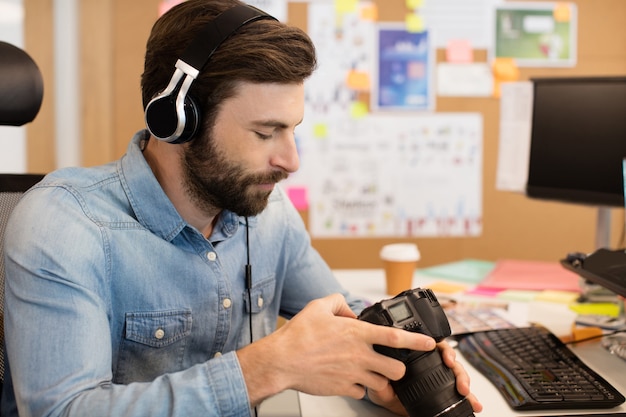 Fotograaf hoofdtelefoon dragen tijdens het gebruik van camera in creatieve kantoor