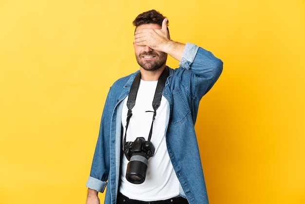 Fotograaf man geïsoleerd op gele achtergrond die ogen bedekt door handen. Wil je iets niet zien