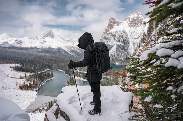 Fotograaf man staande met wandelstokken op sneeuwpiek met uitzicht op de bergen en het meer op het Opabin-plateau in het nationale park Yoho, Canada