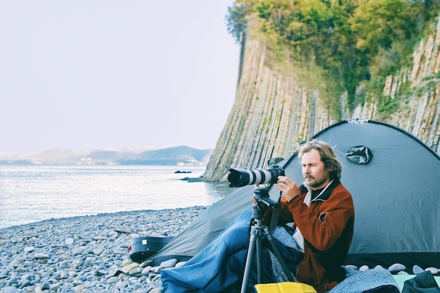 Fotograaftoerist zit in de buurt van tent aan de kust en maakt foto's van landschappen