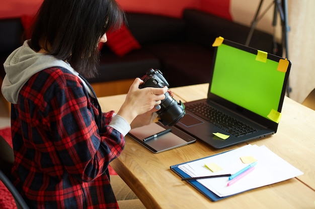 Fotograafvrouw die in een creatief kantoor werkt met camera, aan bureau en retoucheer foto op laptop, retoucheerwerkplek in fotostudio, succesvol freelance artiestenbedrijf, fotografieconcept