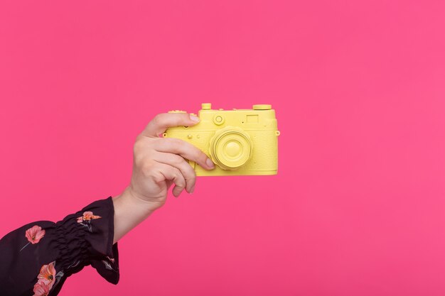 Fotograferen en vintage concept - vrouwelijke hand met gele retro camera op roze muur