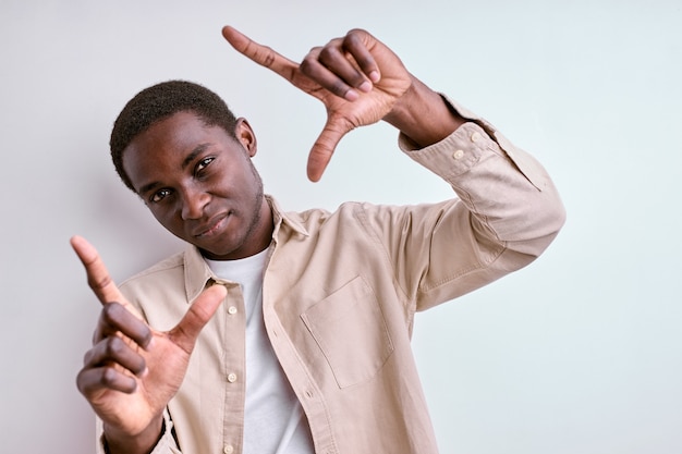 Fotografie concept. Afrikaanse man vierkante vorm uit handen maken, foto nemen. geïsoleerde witte studiomuur