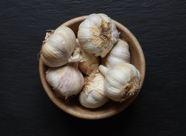 Fotografie van knoflookkoppen in een houten kom op leisteenachtergrond