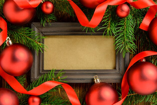 Fotokader tussen kerstmisdecoratie, met rode ballen en linten op een bruine houten lijst. bovenaanzicht, frame om ruimte te kopiëren.