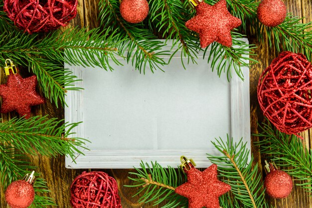 Fotokader tussen Kerstmisdecoratie, met rode ballen en sterren op een bruine houten lijst. Bovenaanzicht, frame om ruimte te kopiëren.