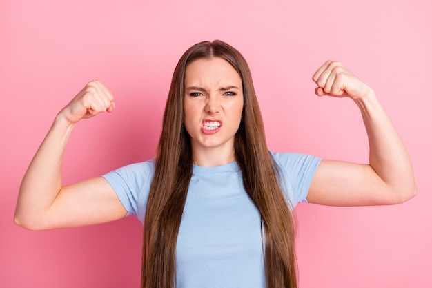 Fotoportret van boze vrouw die buigt met biceps geïsoleerd op pastelroze gekleurde achtergrond