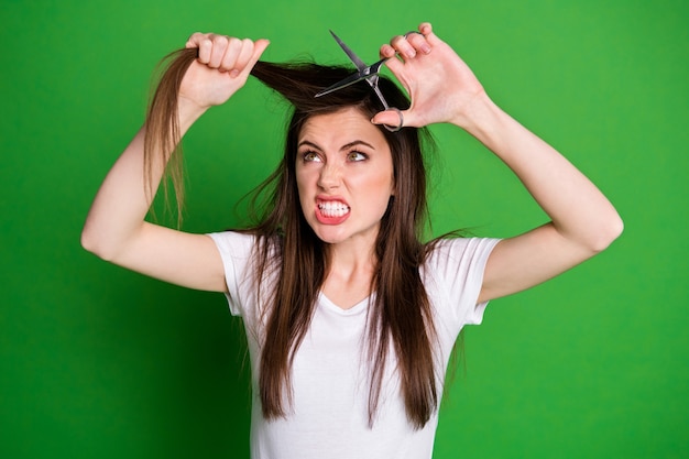 Fotoportret van boze vrouw die haar knippen met een schaar geïsoleerd op een levendige groen gekleurde achtergrond