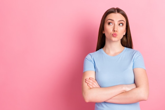 Fotoportret van een pruilende vrouw met gevouwen armen kijkend naar lege ruimte geïsoleerd op pastelroze gekleurde achtergrond