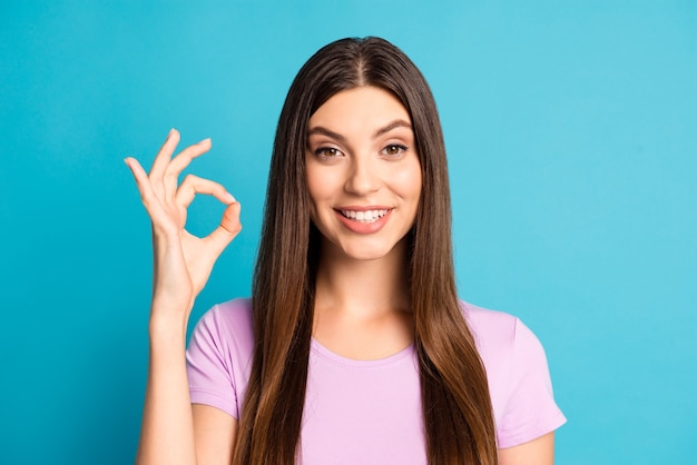 Fotoportret van een schattige, schattige jonge vrouw die een casual violet t-shirt draagt met een okey een arm geïsoleerde blauwe achtergrondkleur