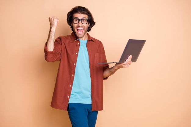 Fotoportret van een vrolijke kerel die een laptop in de hand houdt geïsoleerd op een pastelbeige gekleurde achtergrond