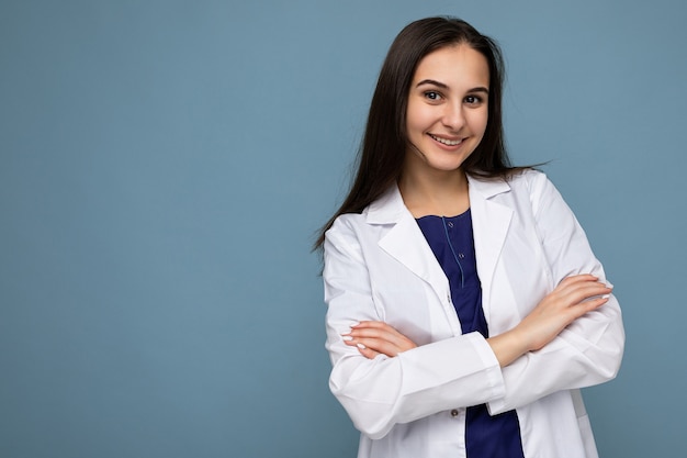 Fotoportret van jonge vrij mooie positieve glimlachende donkerbruine vrouw met oprechte emoties die witte medische jas dragen