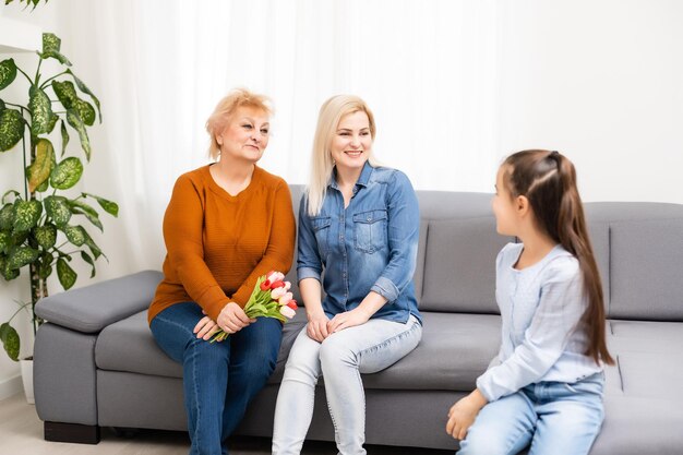 Fotoportret van kleindochter die oma feliciteert die tulpenbos geeft die dichtbij mamma zit.