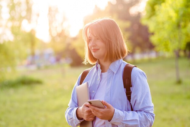 Fotoportret van studente met telefoon en laptop glimlachend buitenshuis in het park