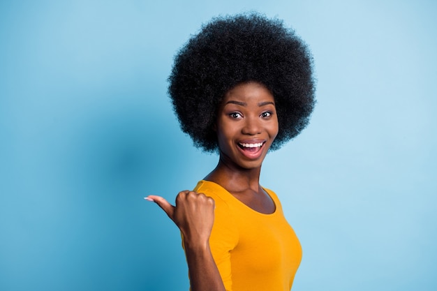 Fotoportret van verrast gelukkig zwart gevild meisje wijzend met de vinger naar lege ruimte glimlachend geïsoleerd op levendige blauwe kleur achtergrond